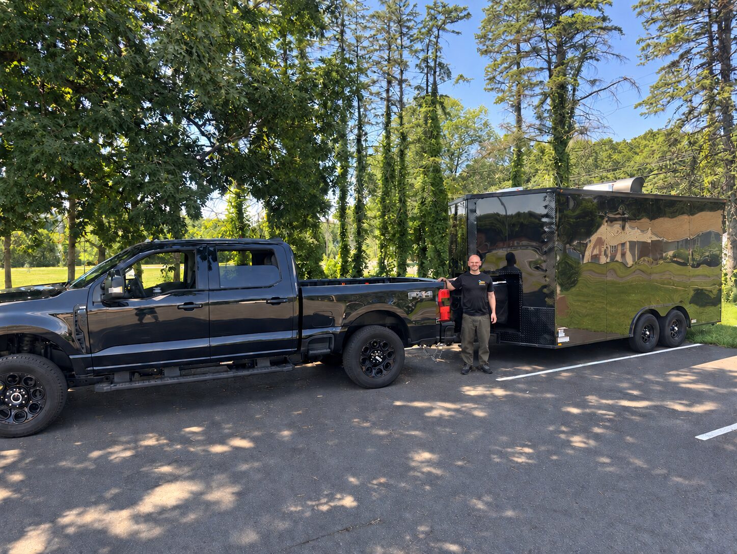 Rim Revival owner standing between the black Ford pickup truck and the enclosed mobile repair trailer